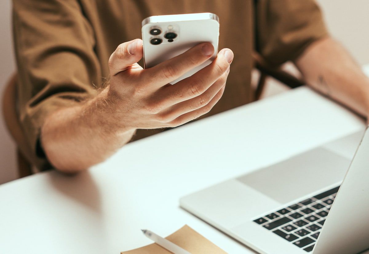 Person using a smartphone beside an open laptop at a desk