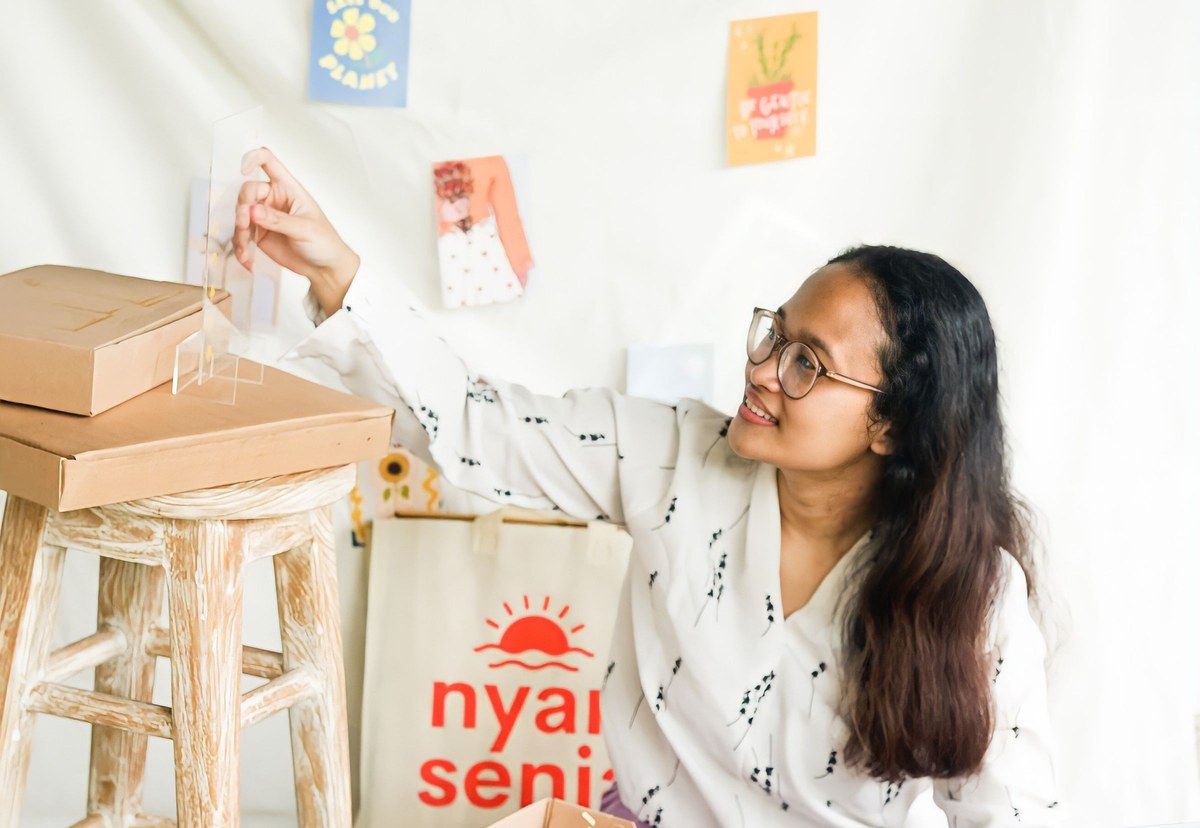 A small business owner preparing products beside stacks of cardboard boxes.