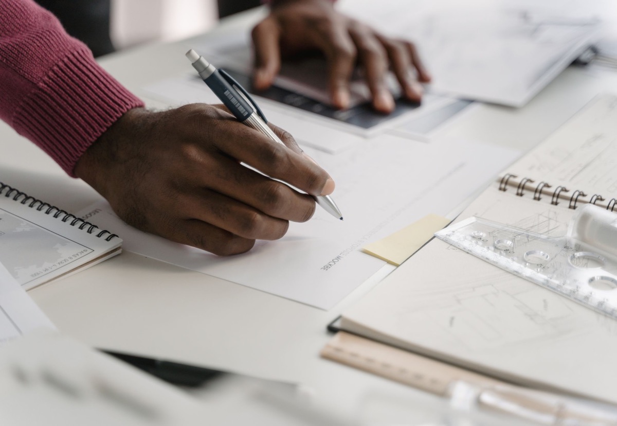 Architect drafting a detailed plan beside a laptop, representing the translation of a working spreadsheet into a structured business system