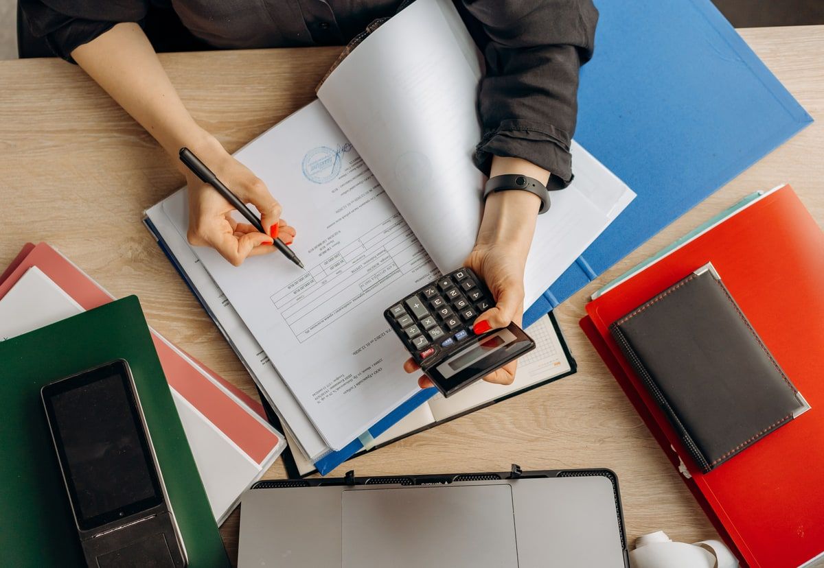 Hands reviewing financial records with a calculator, folders and a laptop on a desk