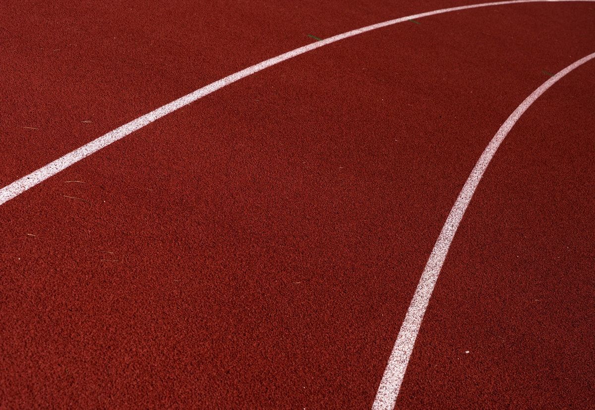 Close up of white lane markings curving across a red athletics track, representing the consistent rhythm and direction of a Scrum sprint