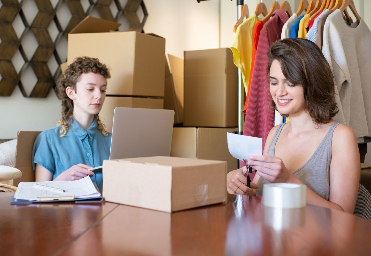 Two people managing an online clothing store beside a laptop, stock and packing boxes.