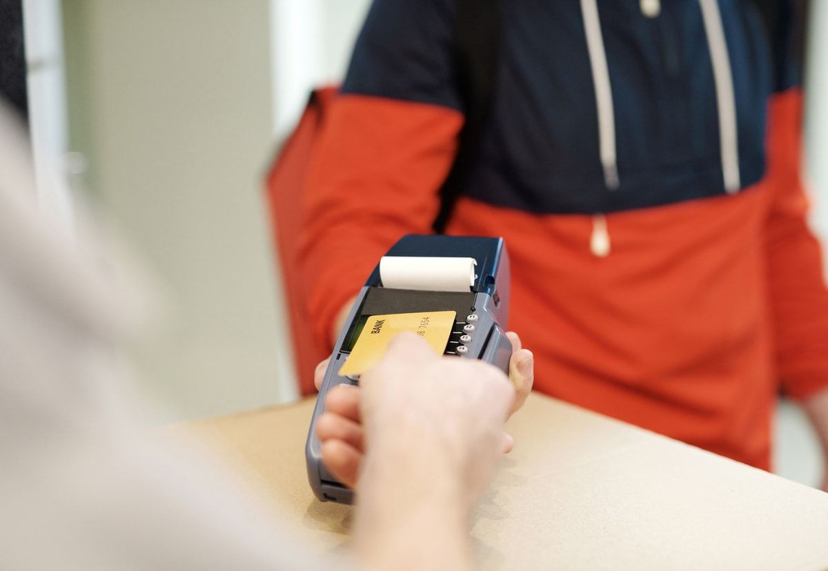 A customer taps a payment card on a handheld card terminal at a shop counter