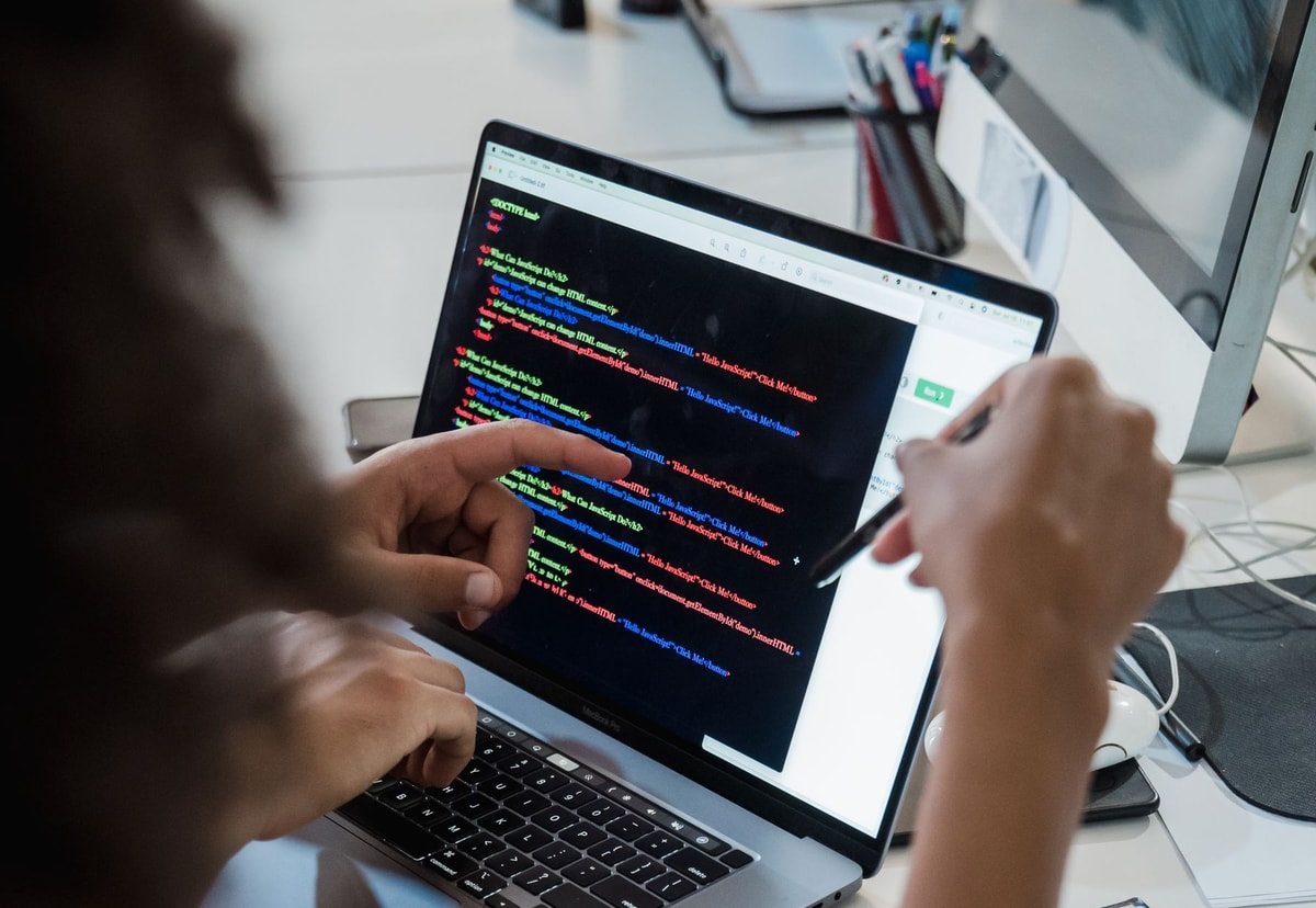 Two software developers pointing at code on a laptop during a code review