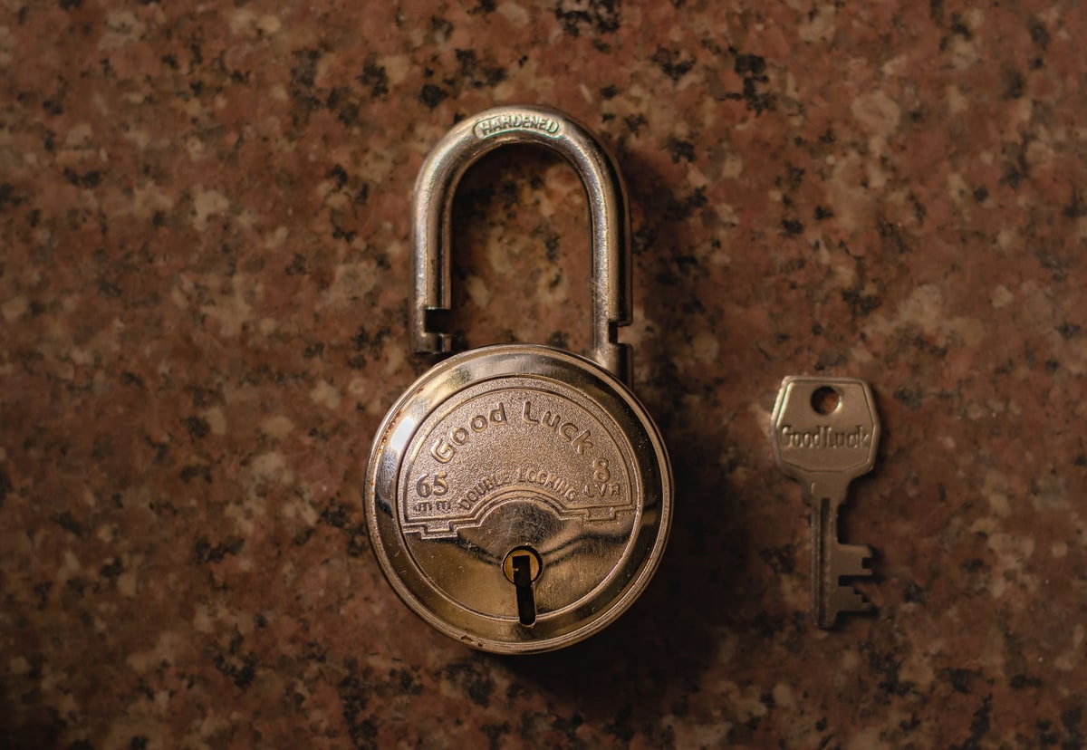 Open brass padlock and matching key on a warm brown stone surface
